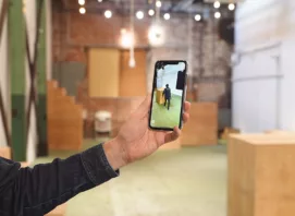 A hand holding a smartphone that displays AR in a space that has a digital twin