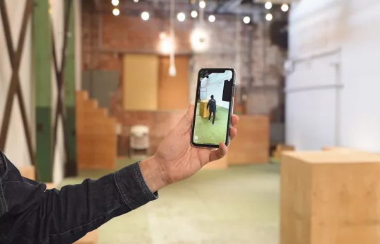 A hand holding a smartphone that displays AR in a space that has a digital twin